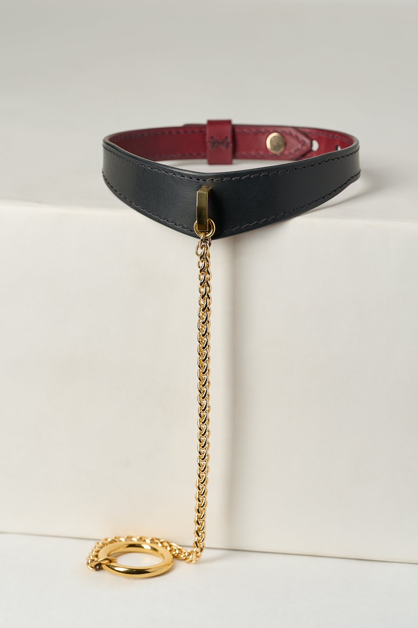 Black leather choker with gold chain and clasp on a white background