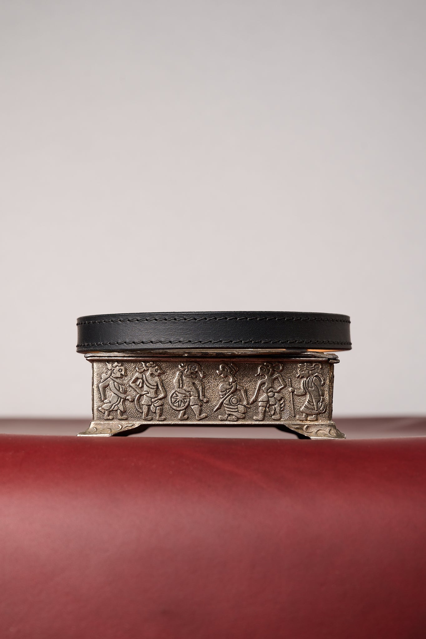 Black leather collar on decorative metal box with embossed designs on a red surface