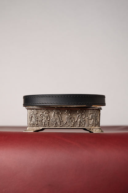 Black leather collar on decorative metal box with embossed designs on a red surface