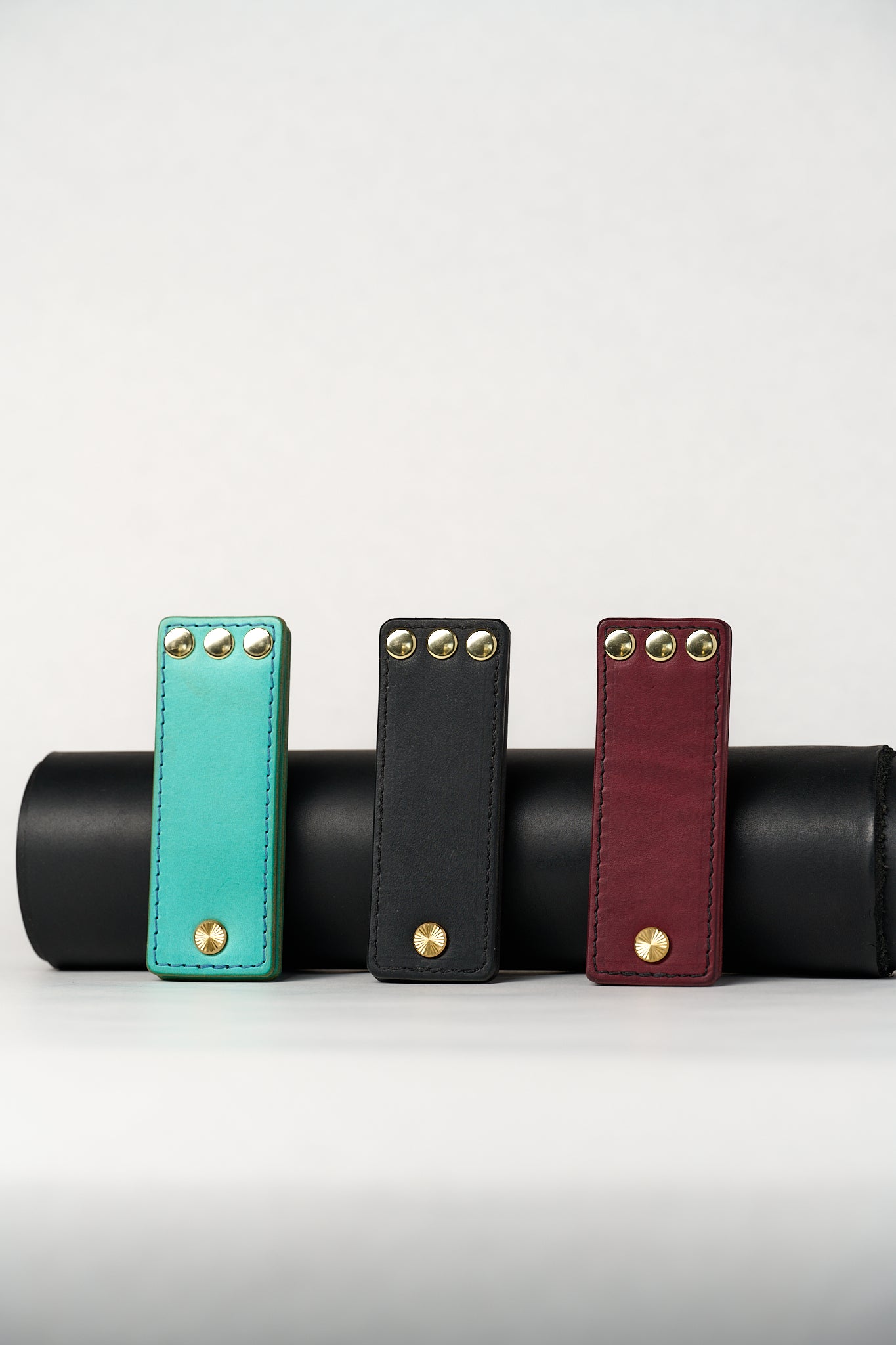 Three leather novelty items in turquoise, black, and red with gold studs on a white background