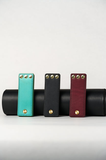 Three leather novelty items in turquoise, black, and red with gold studs on a white background