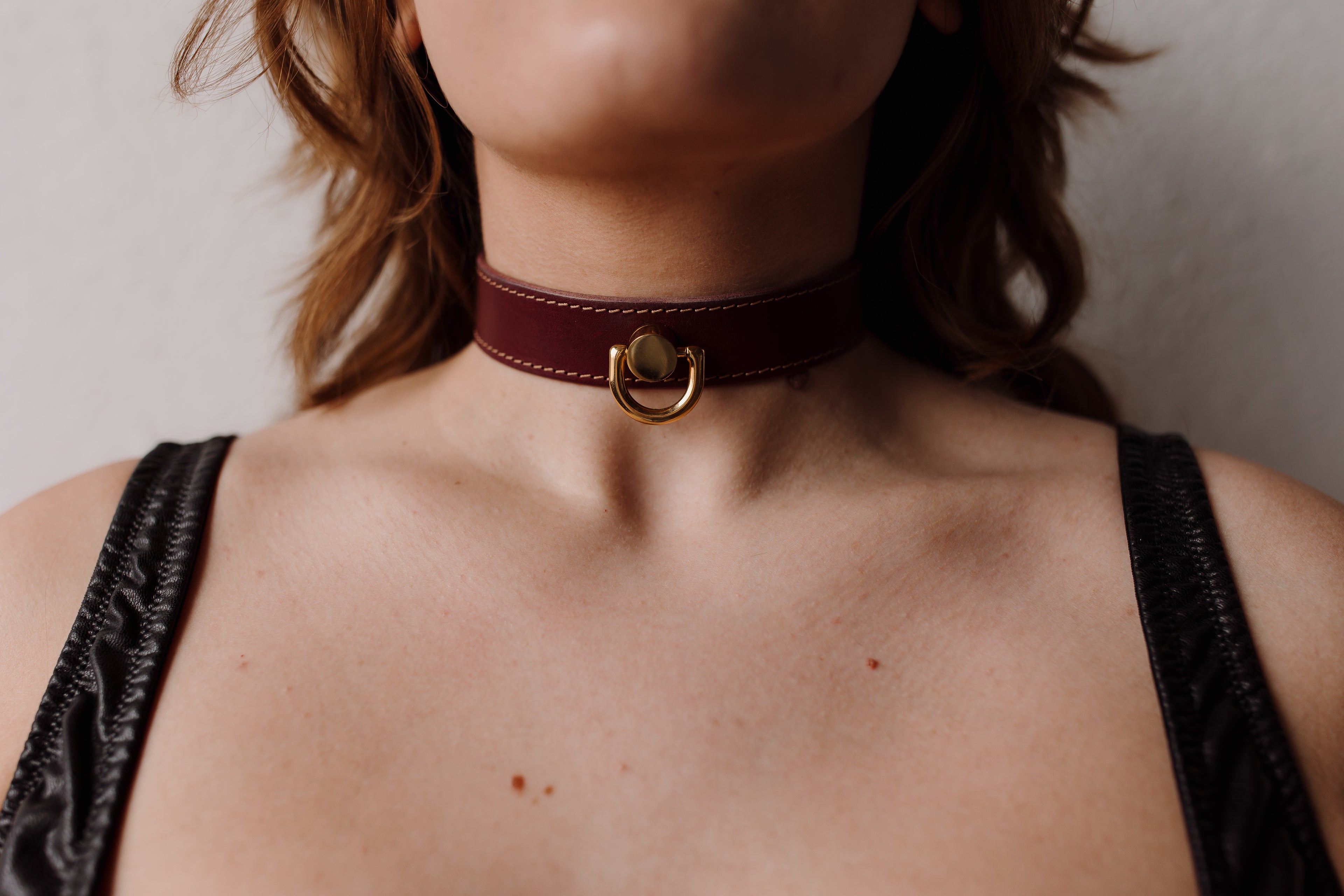 Person wearing a burgundy leather choker with a gold clasp on a neutral background