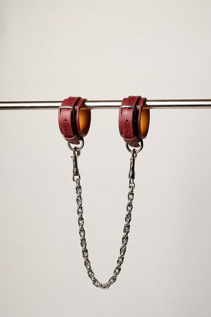 Red leather cuffs with chains on a white background