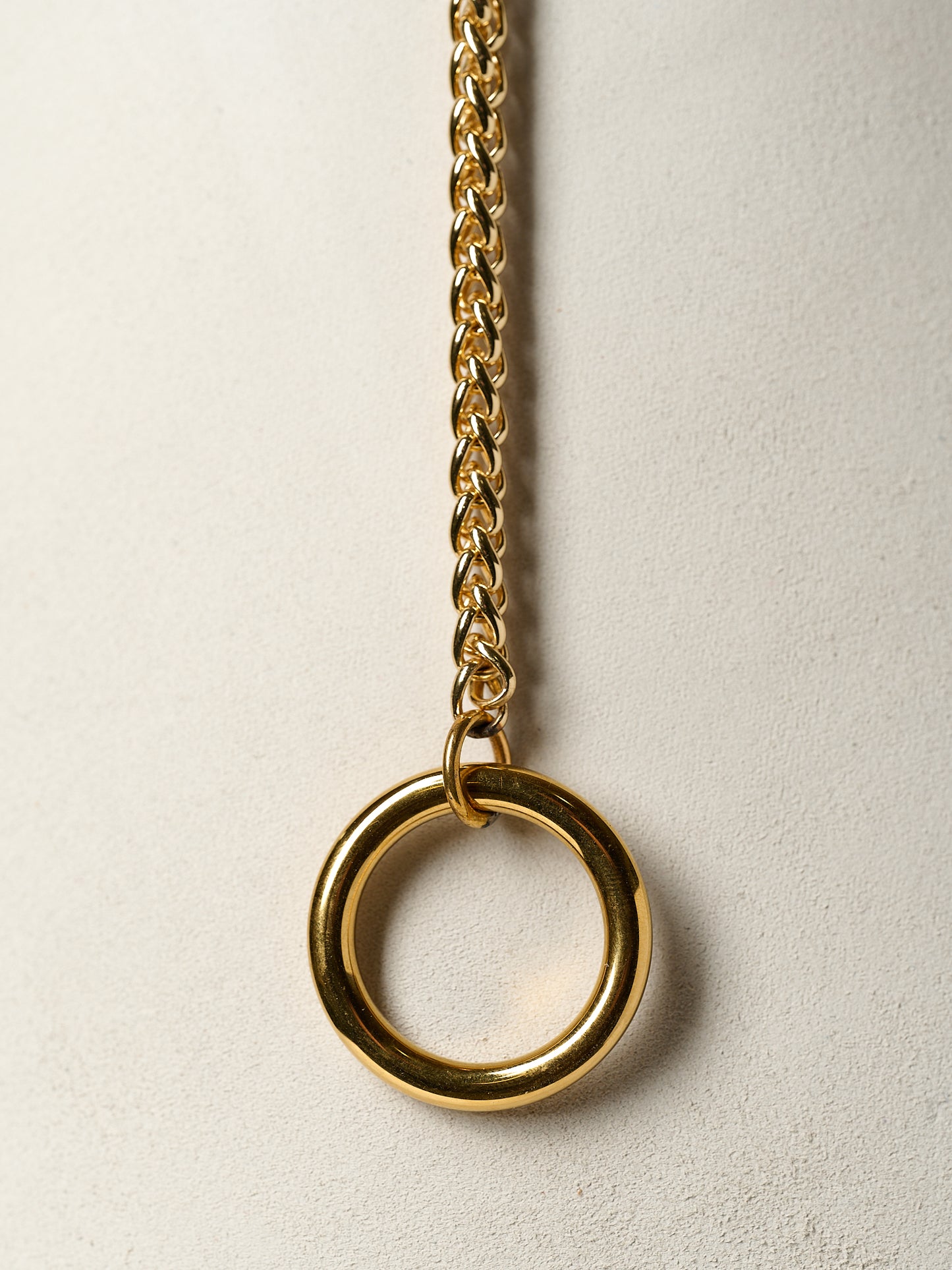 Gold chain necklace with a large ring pendant on a light beige background