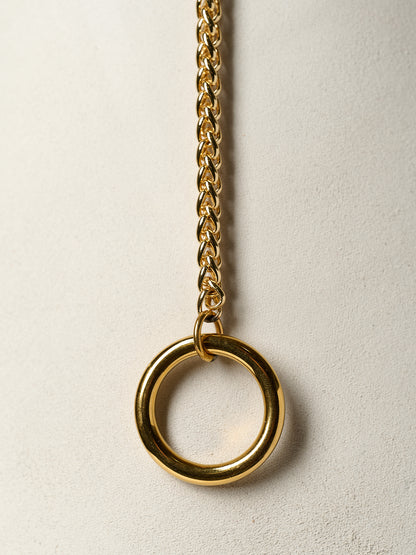 Gold chain necklace with a large ring pendant on a light beige background