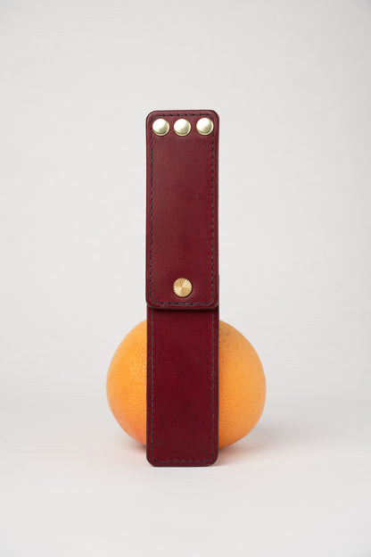 Burgundy leather portable pocket paddle with brass rivets and black thread.