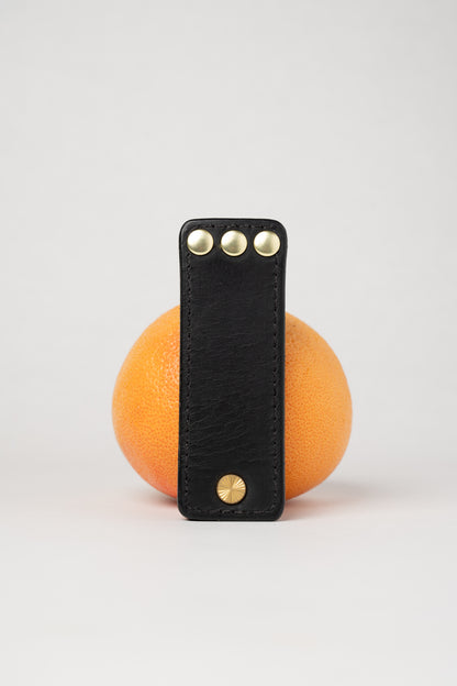 Black leather portable pocket paddle with brass rivets and black thread.