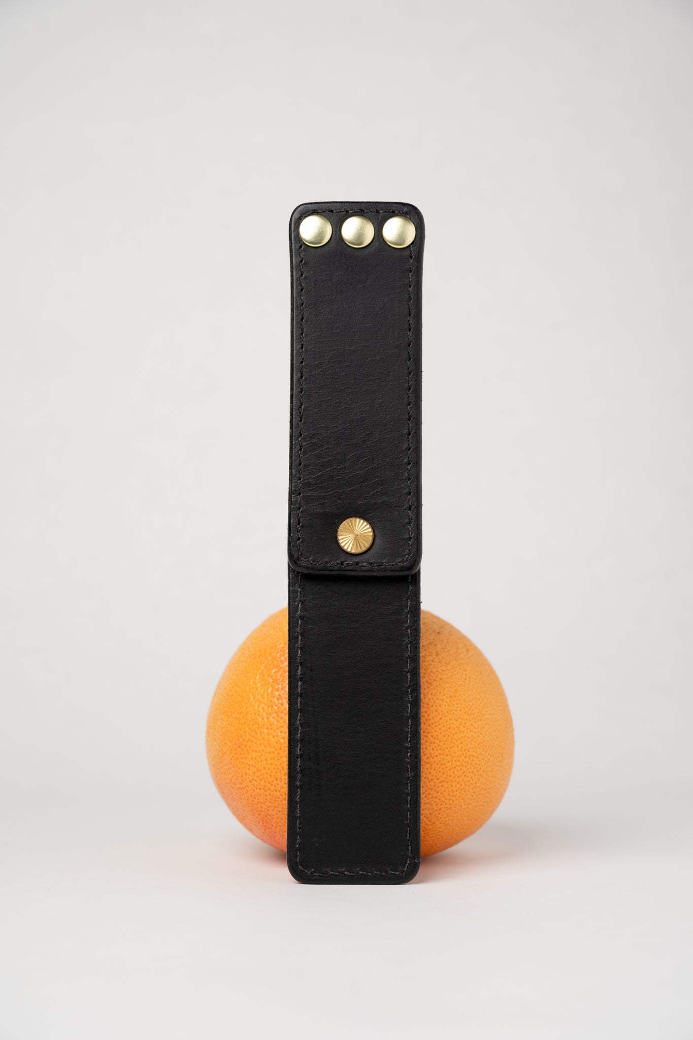 Black leather portable pocket paddle with brass rivets and black thread.