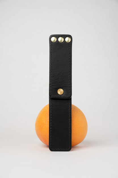 Black leather portable pocket paddle with brass rivets and black thread.