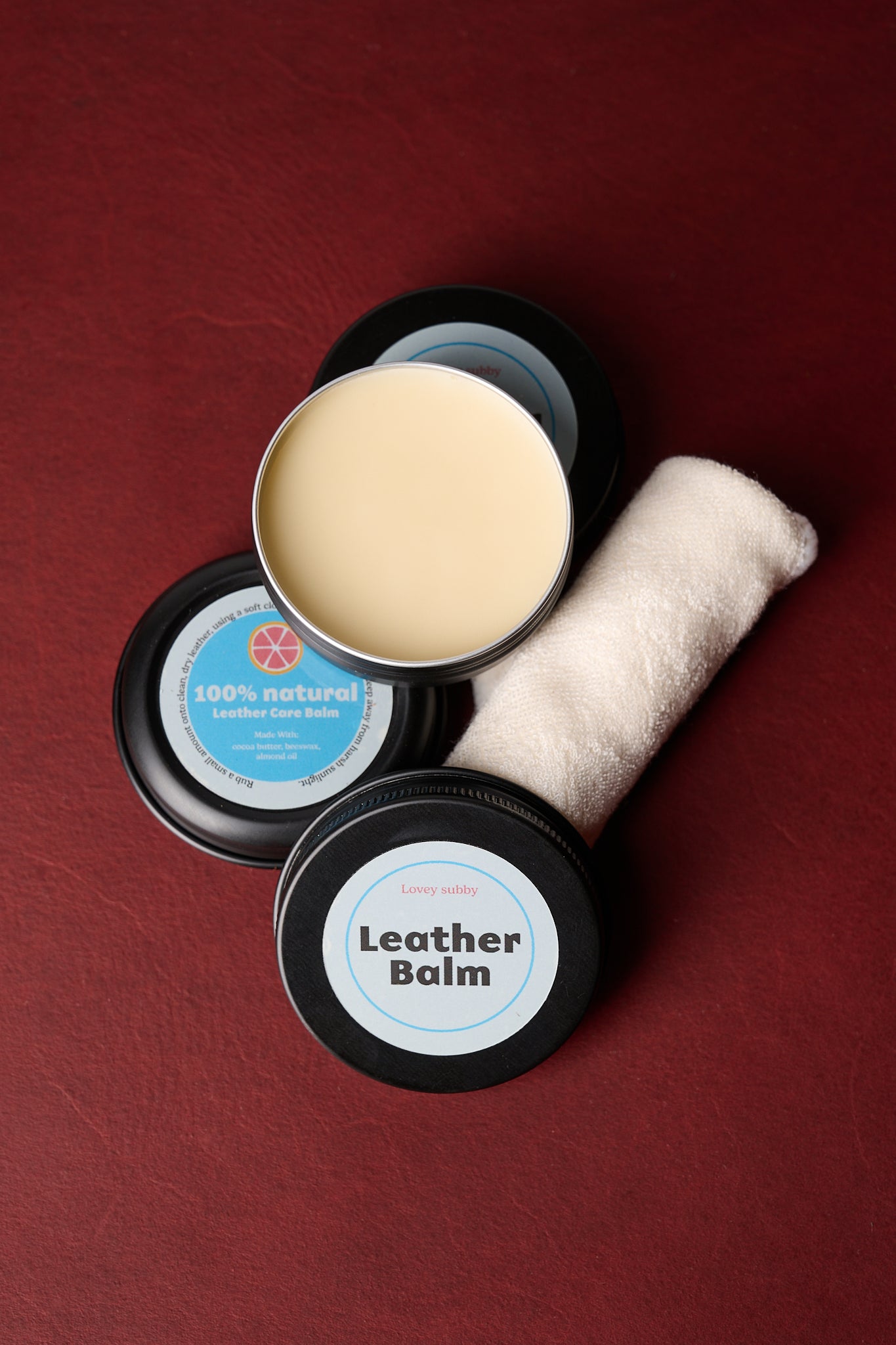 Natural handmade leather conditioning balm with applicator cloth on a red background