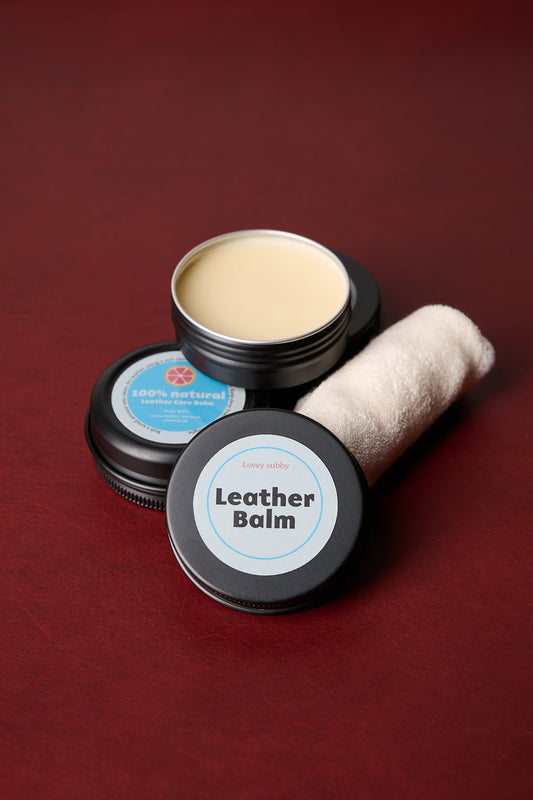 Two containers of handmade leather conditioning balm with a cloth on a red background