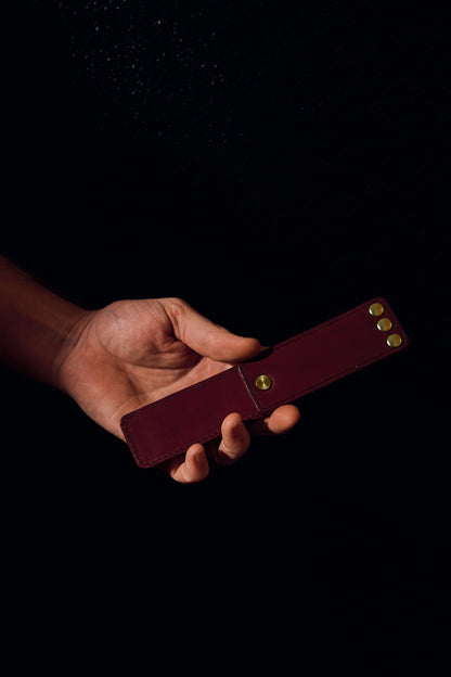 Lovey Subby burgundy/pomegranate leather portable pocket paddle with brass rivets and black thread in a mans hand.