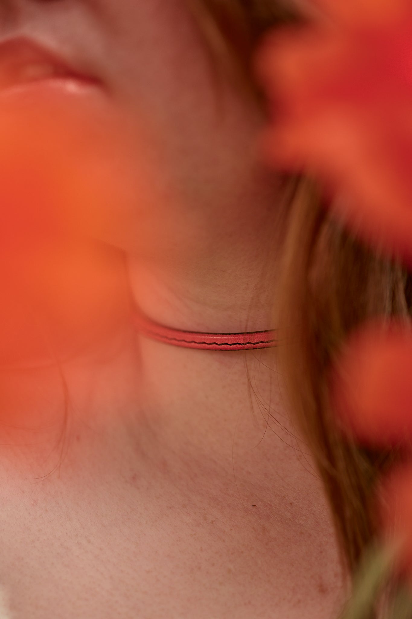 Close-up of a person's neck with a thin pink necklace, surrounded by blurred orange flowers.