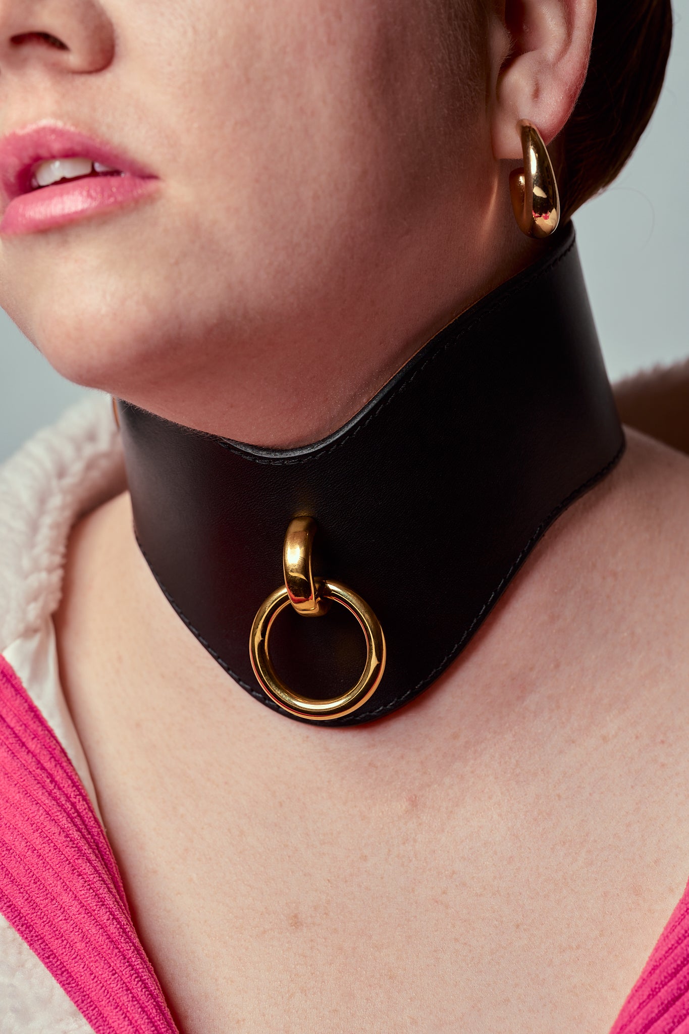 Person wearing a tall black necklace with gold rings on a neutral background